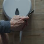 Persona sentada en el baño con el teléfono en la mano, con una expresión de alerta y preocupación
