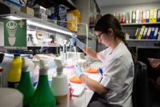 Imagen de un médico especialista en oncología trabajando en un laboratorio con microscopios y equipo de investigación.