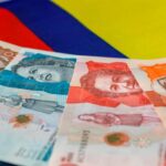 Una persona sostiene un billete de peso colombiano con un gráfico de aumento de valor detrás
