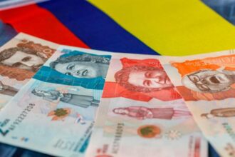 Una persona sostiene un billete de peso colombiano con un gráfico de aumento de valor detrás