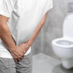 Imagen de una persona en una reunión con una expresión de incomodidad, con una mano en la espalda baja, sugiriendo dolor o molestia.